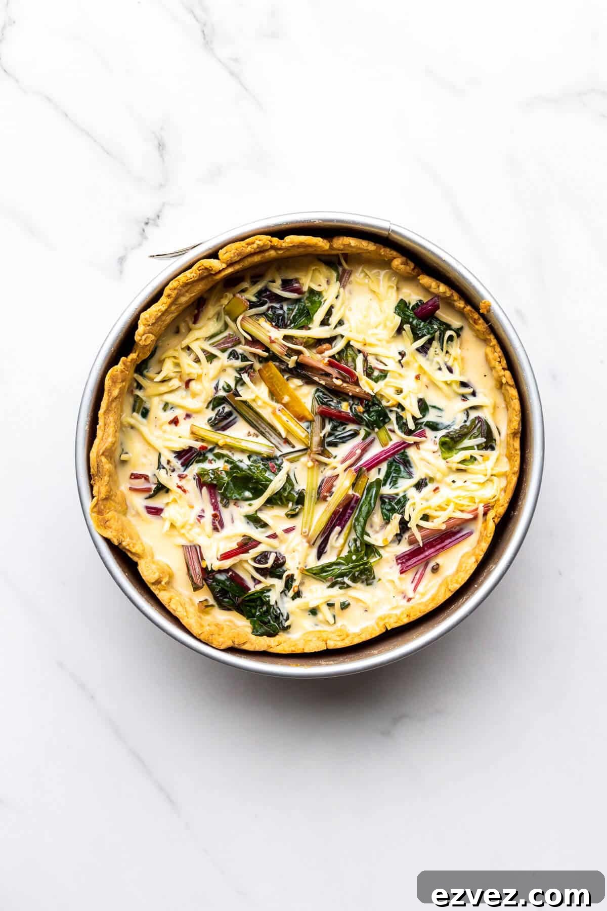 A blind baked pie crust in a 9 inch springform pan filled with a savoury custard, Swiss chard, and shredded cheese, ready to be baked.