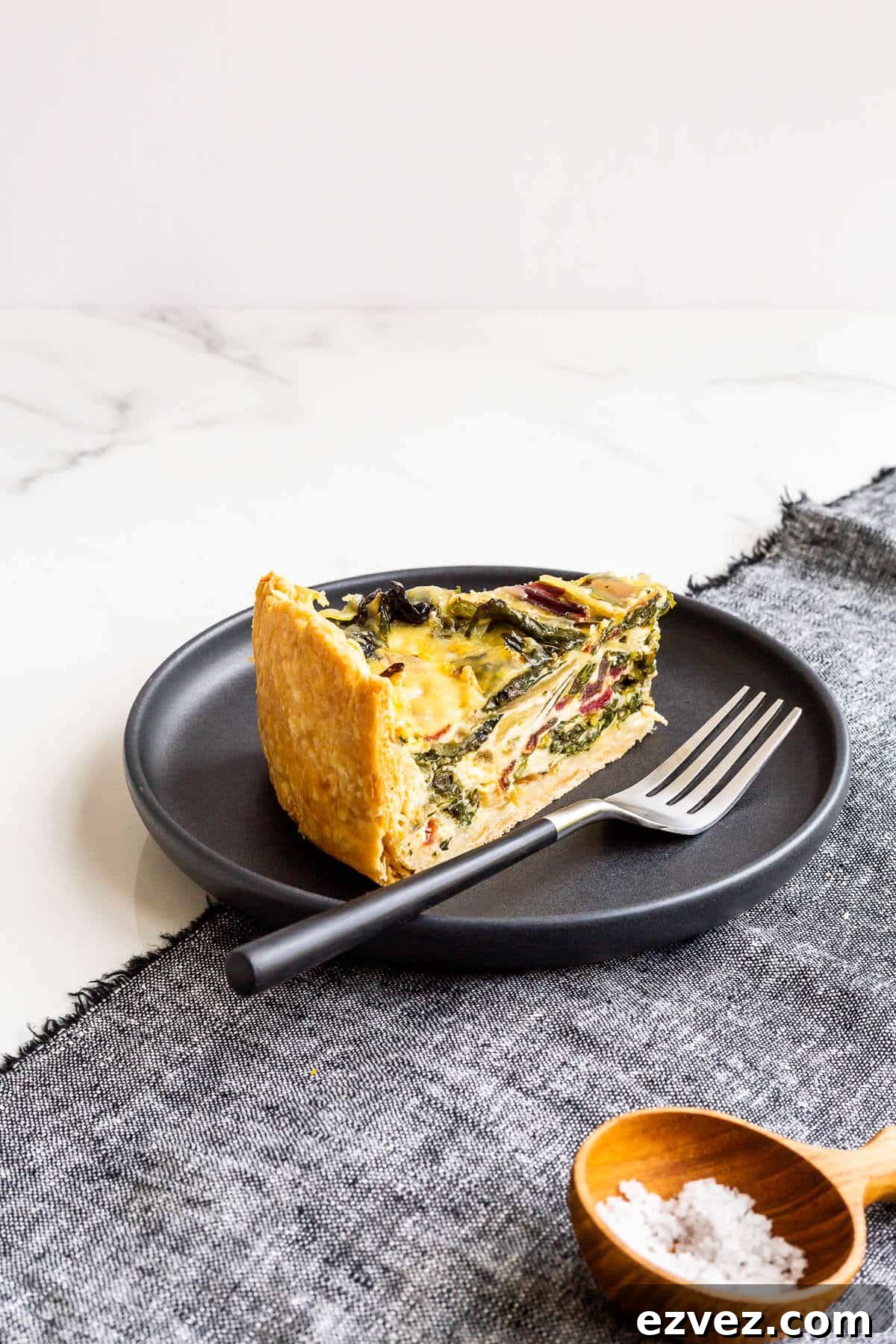 A slice of quiche with rainbow Swiss chard in it, served with a small bowl of salt on the side.