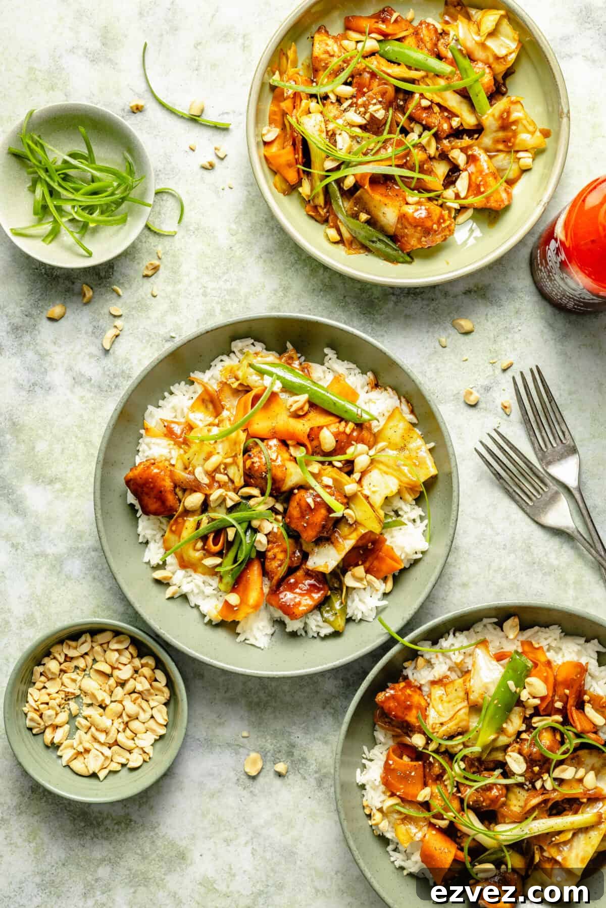 plated spicy Sriracha chicken over white rice and garnished with chopped peanuts and green onions