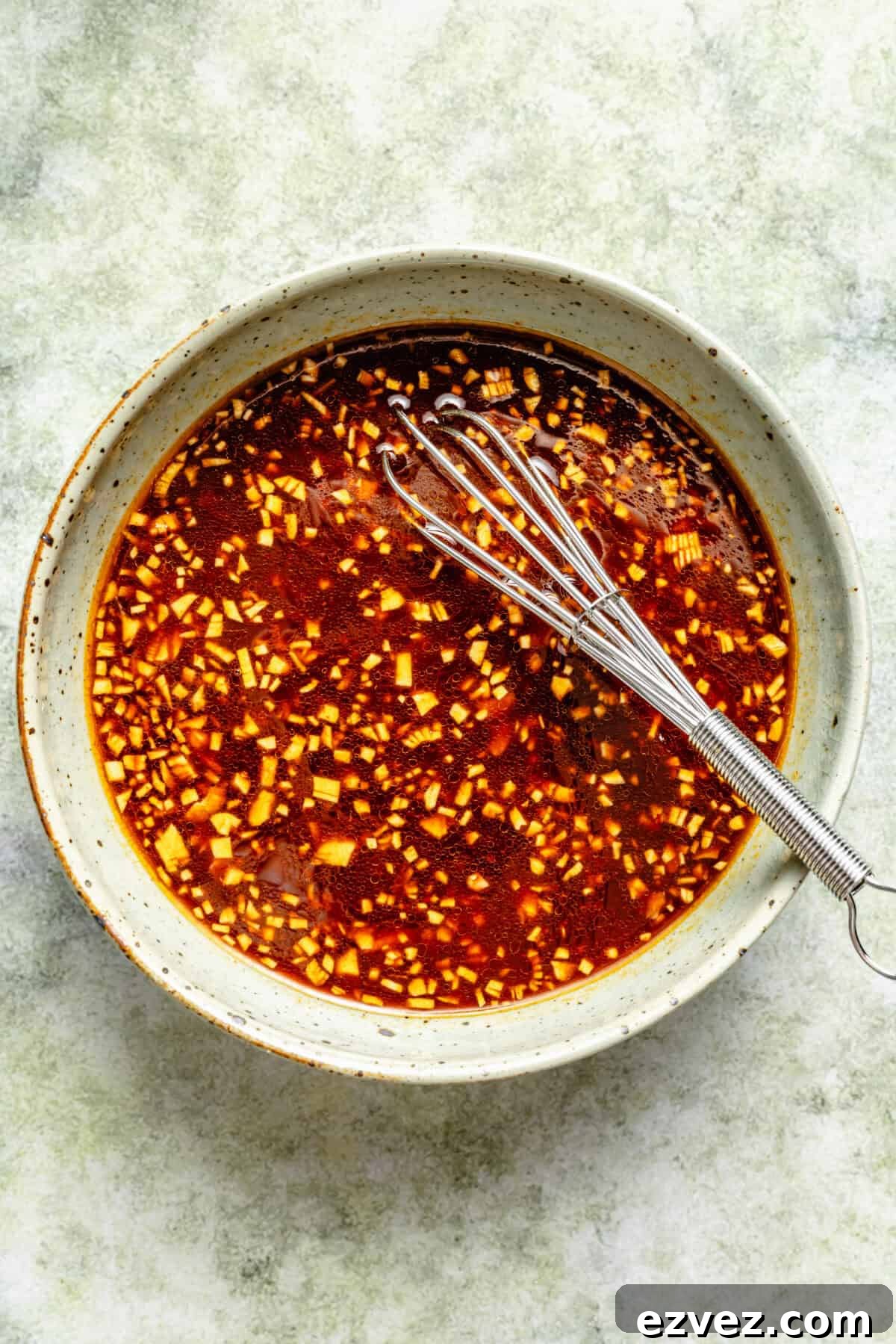 a shallow bowl of a spicy Sriracha sauce with a small stainless steel whisk