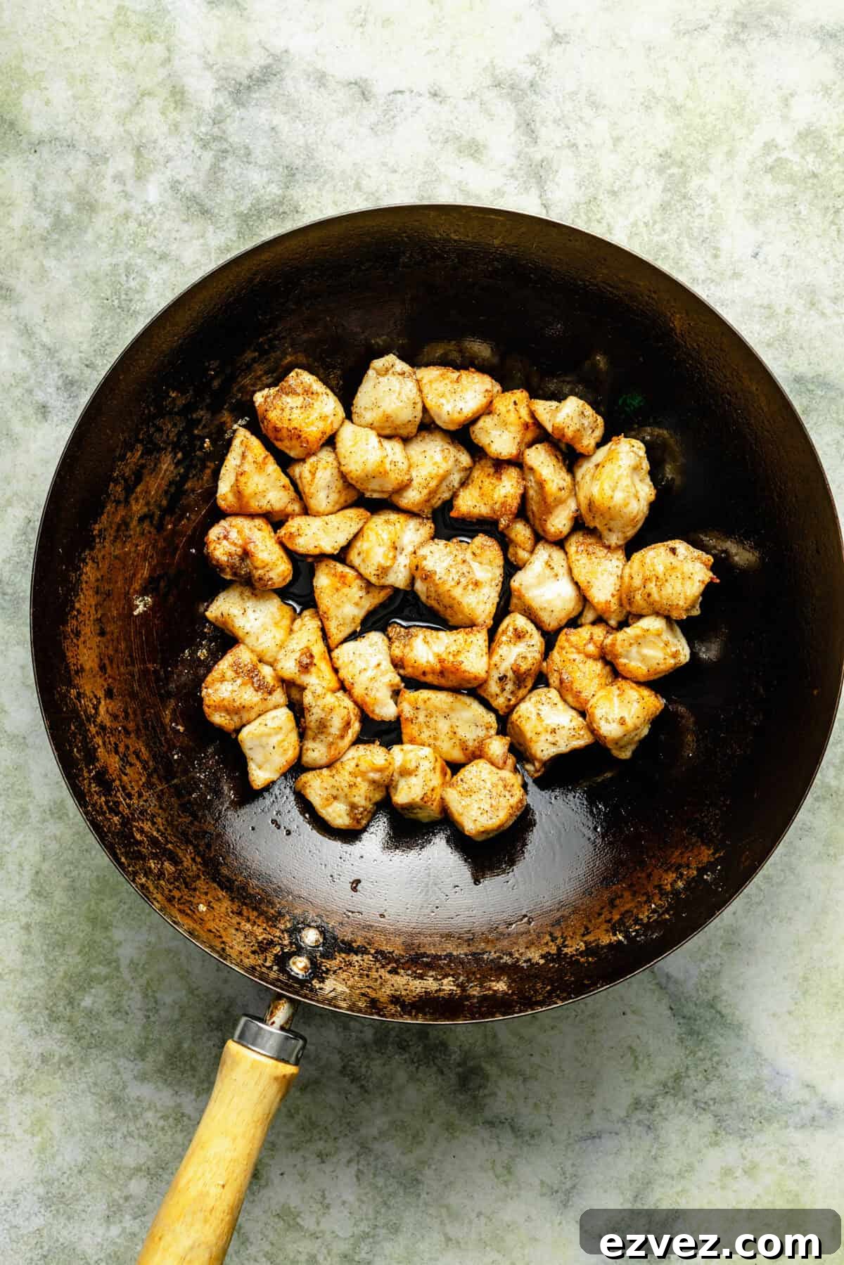 cubed and cooked chicken in a dark skillet on a light green background