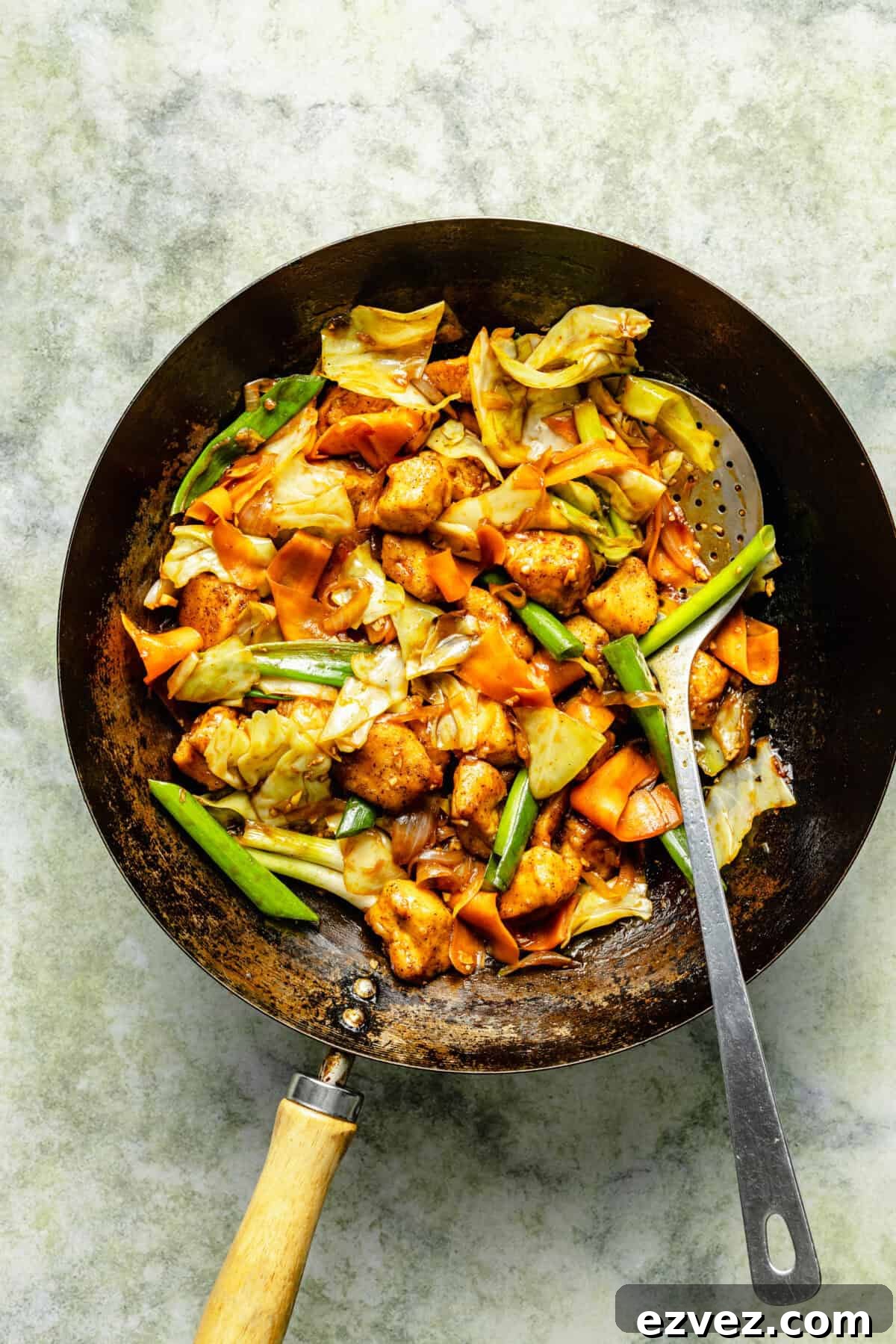 a dark skillet with chicken and vegetables, along with a long stainless steel spoon