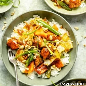 an up-close photo of a light green bowl with white rice, spicy Sriracha chicken, chopped peanuts, and green onions
