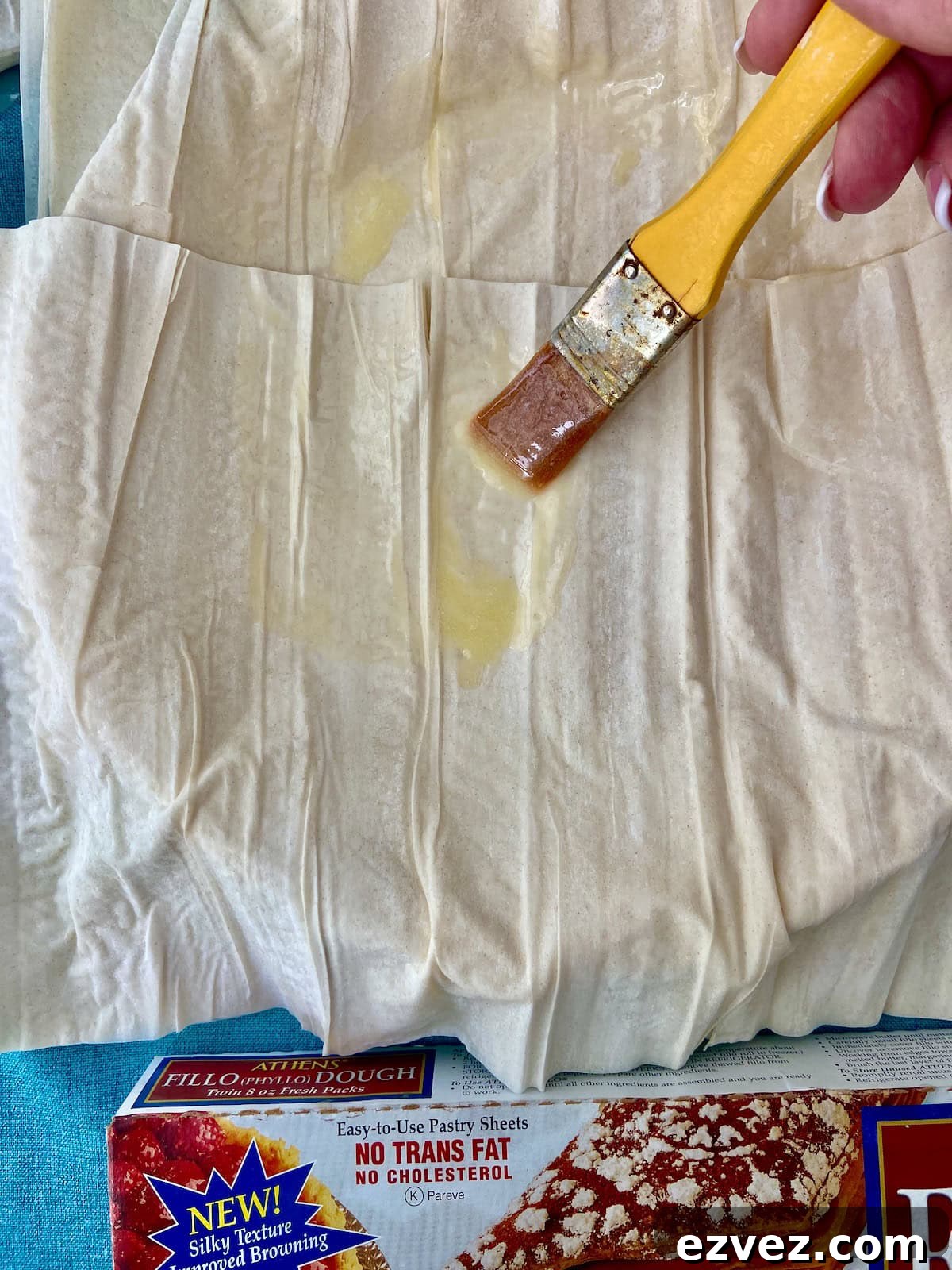 Phyllo dough being brushed with melted butter with pastry brush.