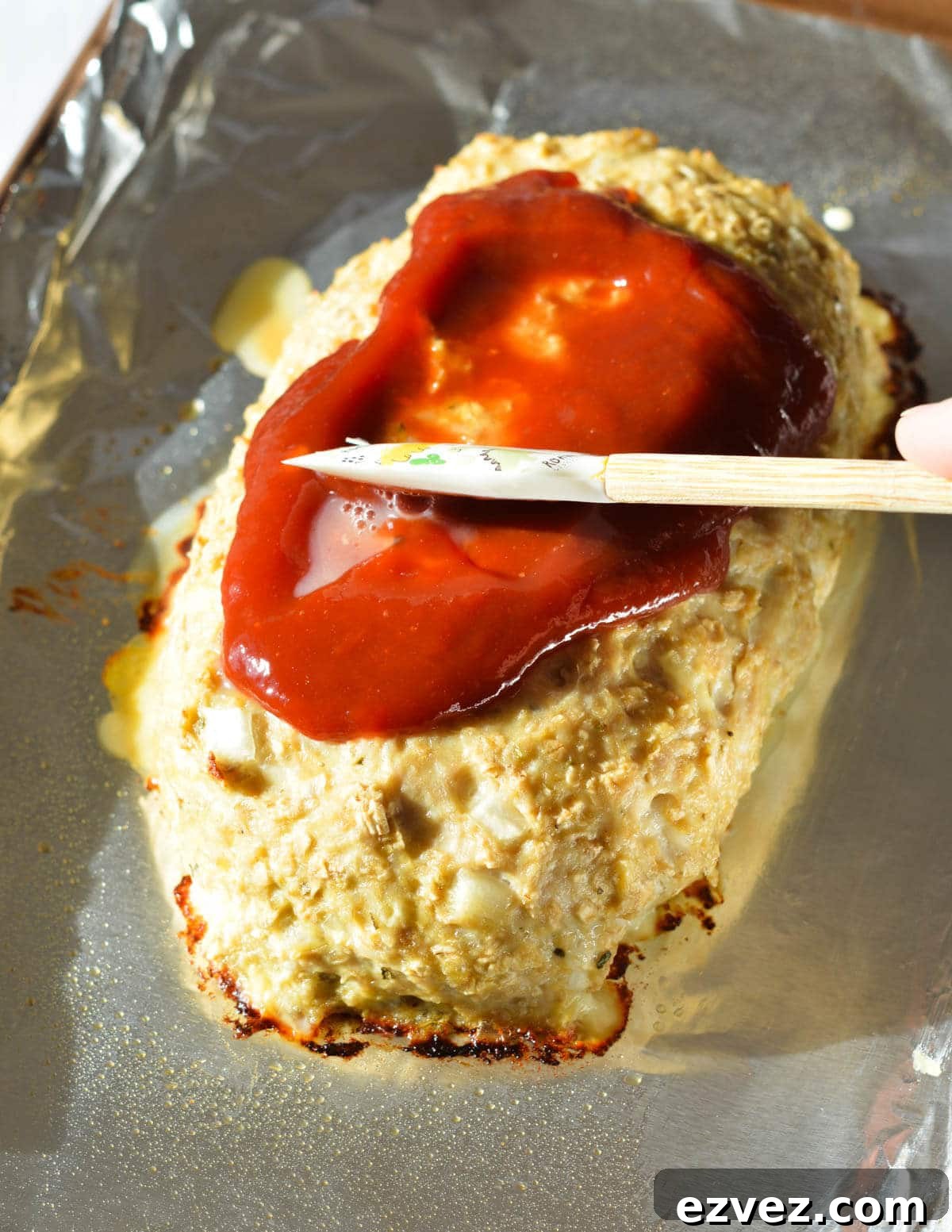 spreading ketchup glaze onto a chicken meatloaf 