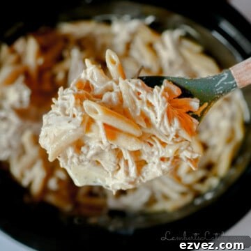 spoonful of crockpot olive garden chicken pasta held above a slow cooker.