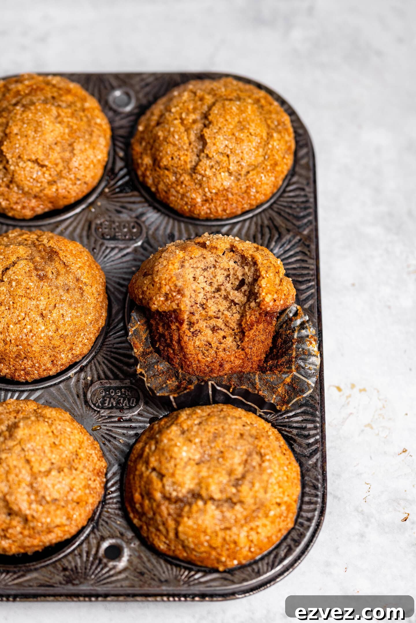 Banana muffins inside a muffin pan with one muffin missing a bite and showing off the interior