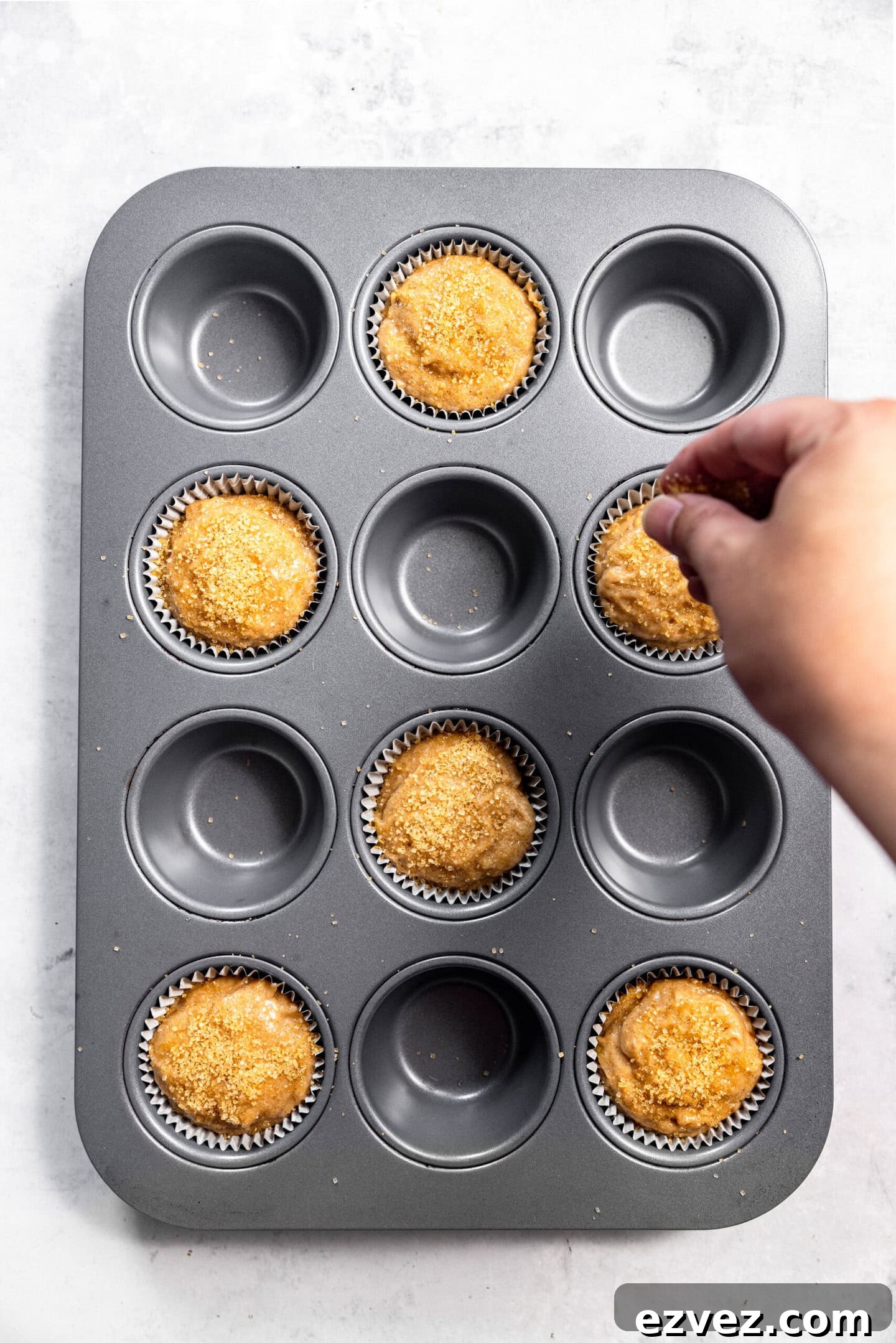 Turbinado sugar being sprinkled on top of muffin batter