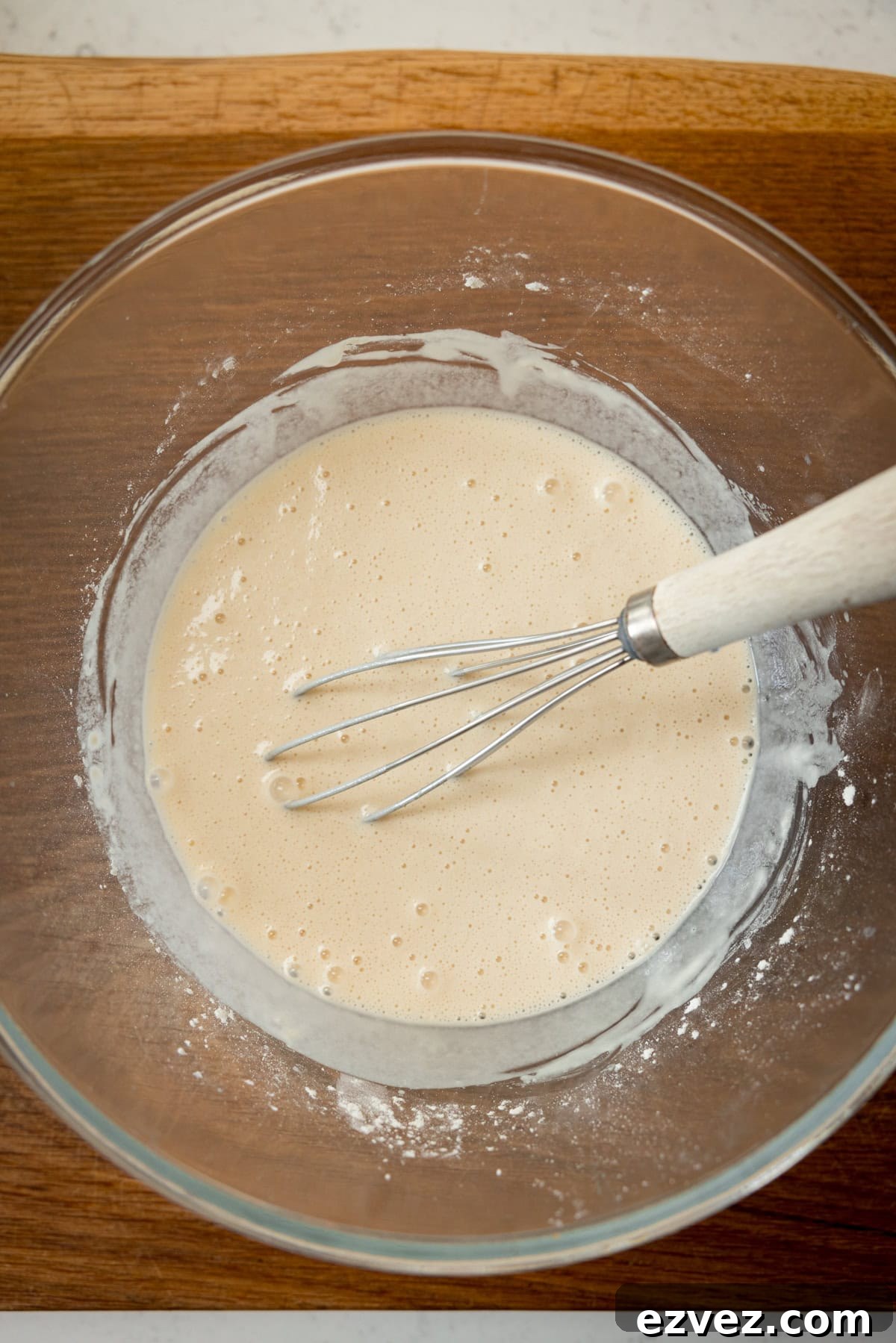 Crispy Beer Batter Recipe for Perfect Fried Fish and Vegetables 2 A tall, overhead shot of the finished beer batter. The batter is in a clear, glass bowl with a whisk wooden handle in the batter. All this is laid on a wooden board.
