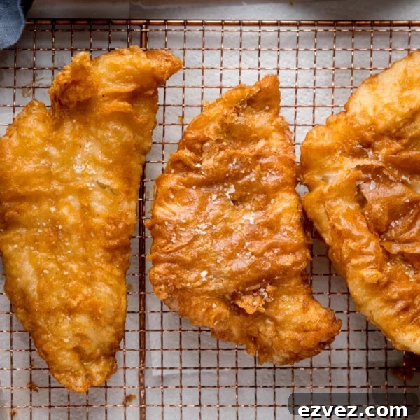 Crispy Beer Batter Recipe for Perfect Fried Fish and Vegetables 5 Three golden beer-battered fish fillets on a wire rack.
