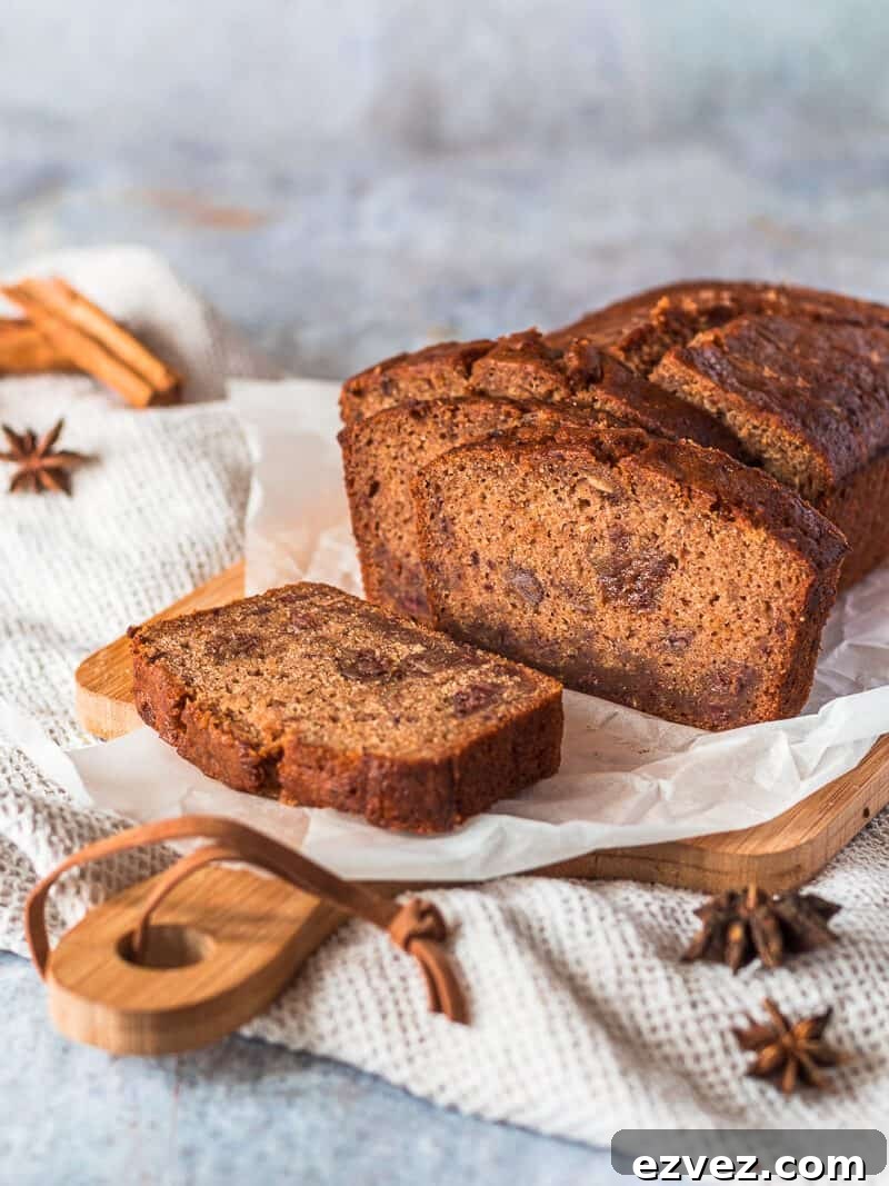 Classic Fruitcake Loaf Recipe for Moist Holiday Bread 2 A Fruit Cake Loaf on a sheet of white baking parchment paper on a wood cutting board. There are some whole spices in the background.