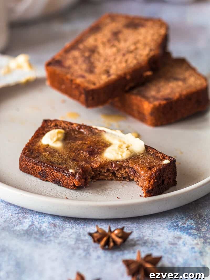 Classic Fruitcake Loaf Recipe for Moist Holiday Bread 4 Three slices of fruit cake loaf on a plate. Two slices are in the background, the slice in front is in focus, a bite has been taken and there is a layer of vegan butter spread onto it - it's melting!