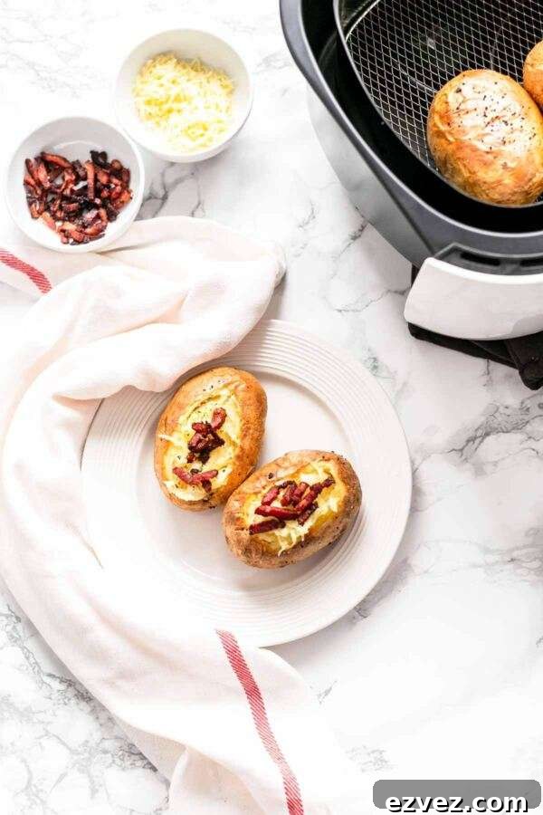 Crispy Air Fryer Baked Potatoes in 30 Minutes 8 Potatoes baked in an Air Fryer presented on a white plate and topped with shredded cheese and grilled bacon.