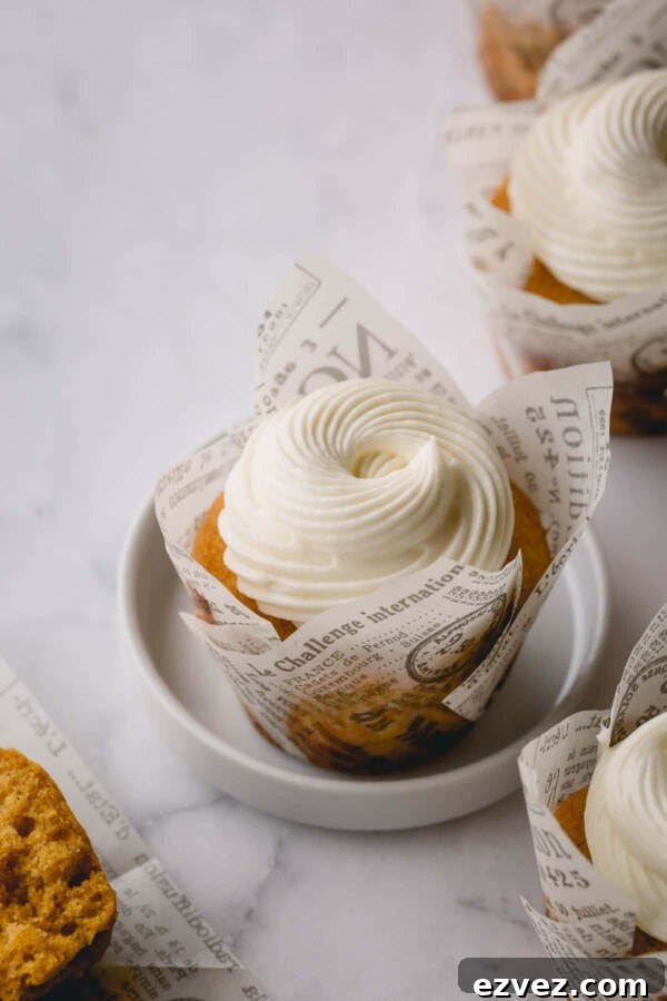 Pumpkin cupcake on a small white plate and topped with cream cheese frosting and surrounded with other cupcakes.
