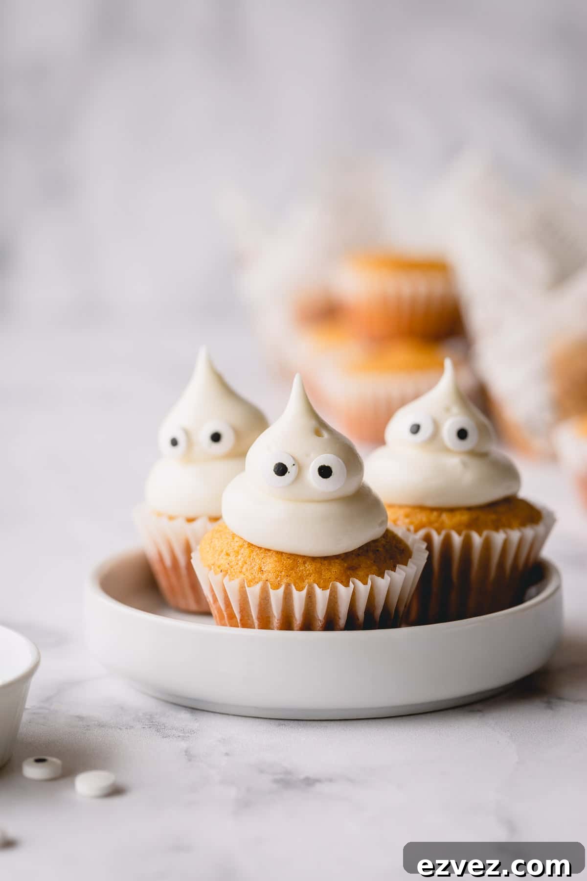 3 mini pumpkin muffins on a white plate topped with domed cream cheese frosting and candy eyes.