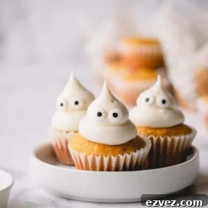 3 mini pumpkin muffins on a white plate topped with domed cream cheese frosting and candy eyes.