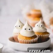 3 mini pumpkin muffins on a white plate topped with domed cream cheese frosting and candy eyes.