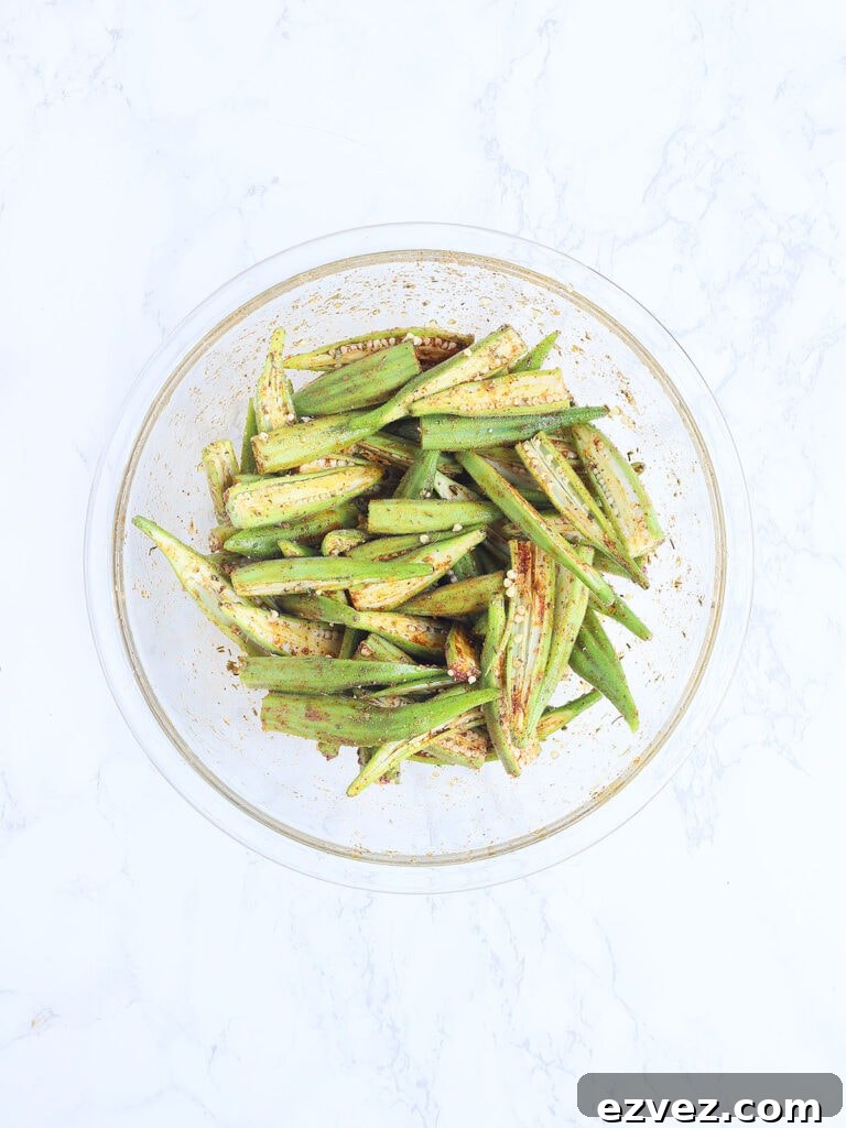 Sliced okra tossed with the seasoning mixture in a glass mixing bowl.
