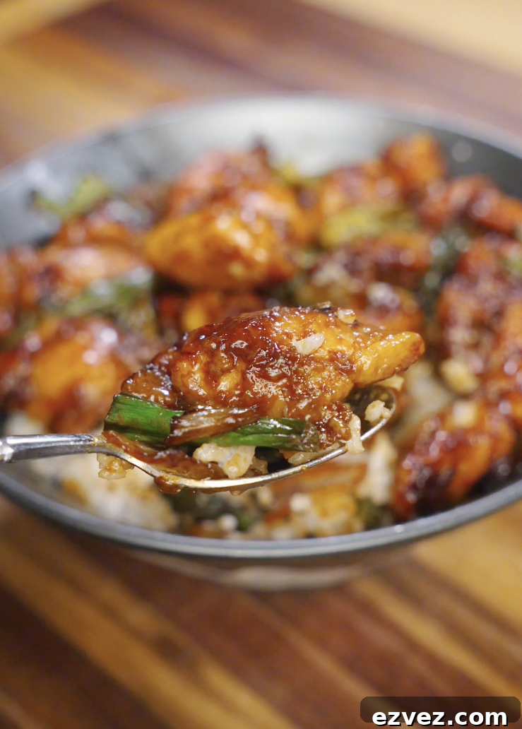 Close up of Mongolian chicken served over white rice, featuring glossy sweet soy glazed chicken thighs, charred onions, and scallions in a shallow bowl.