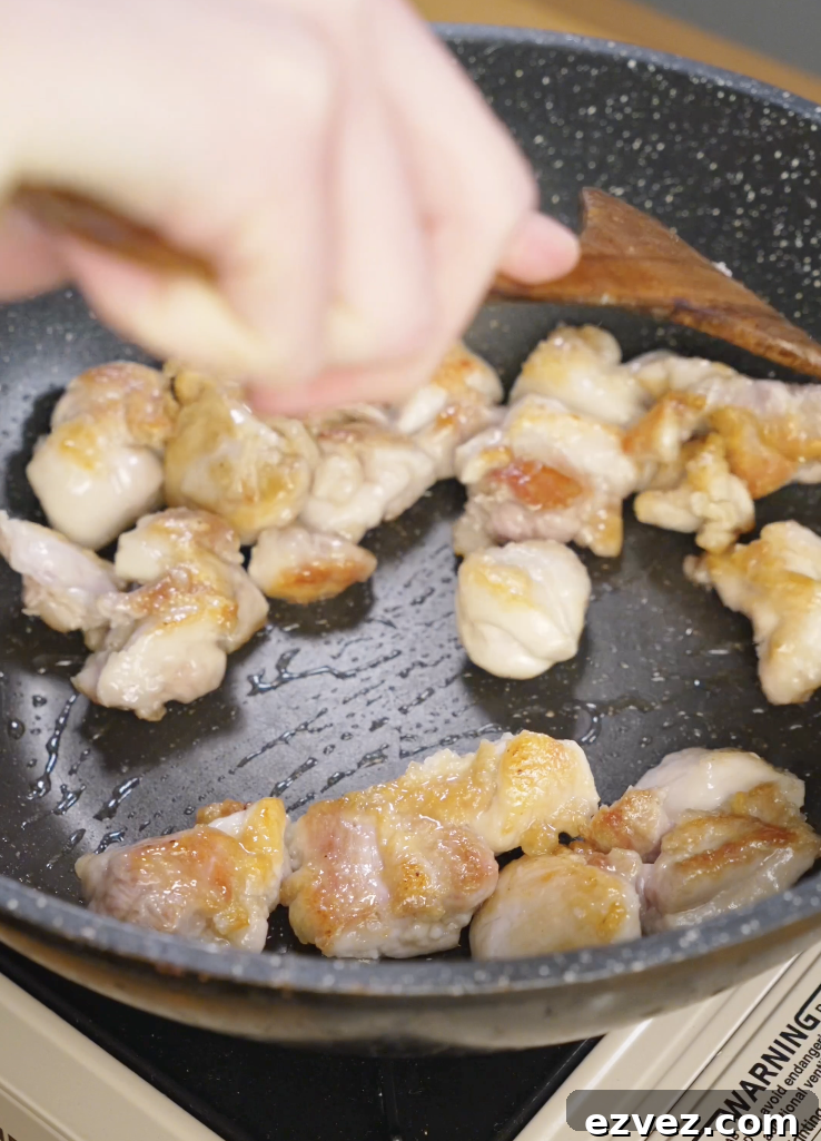 Marinated chicken thigh pieces searing in a hot skillet with oil, developing golden brown edges for Mongolian chicken.