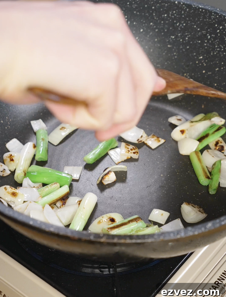 Onion chunks and scallion whites cooking in a skillet until lightly charred to build flavor for Mongolian chicken.