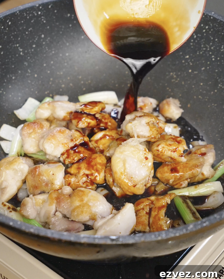 Dark sweet soy based Mongolian sauce being poured over seared chicken thighs and vegetables in a skillet to thicken and glaze.