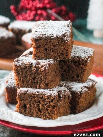 Stack of several gingerbread cake squares on a white plate dusted with powdered sugar.