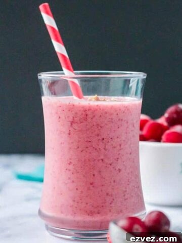 Vibrant red speckled cranberry smoothie in a glass with a red and white straw.