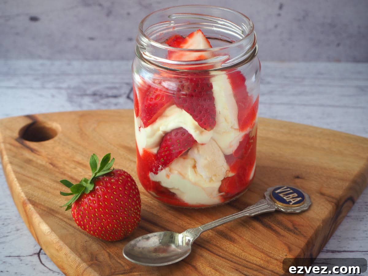 Jar of Eton mess on a board, with strawberry on the side and spoon.