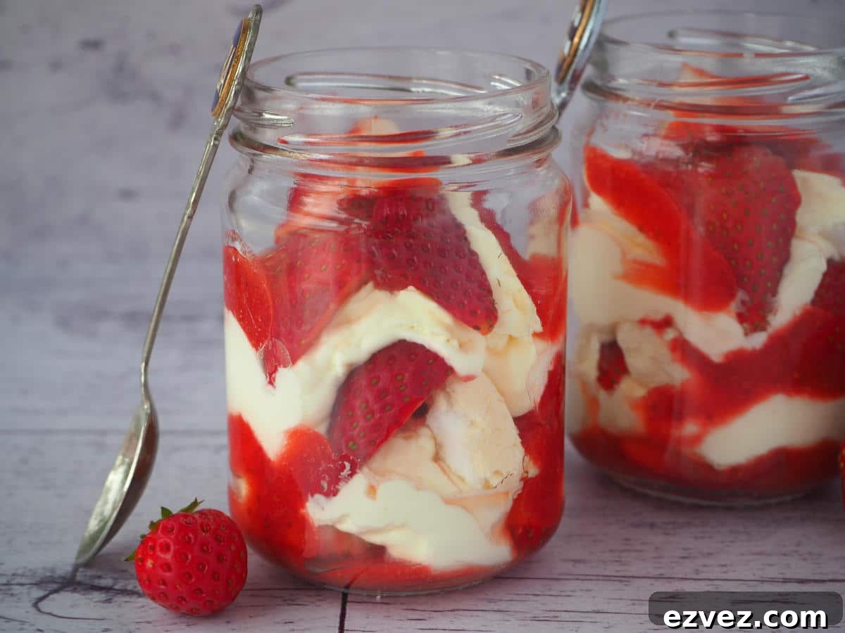 Two jars of Eton mess with fresh strawberries on the side and vintage spoons leaning against the jars.