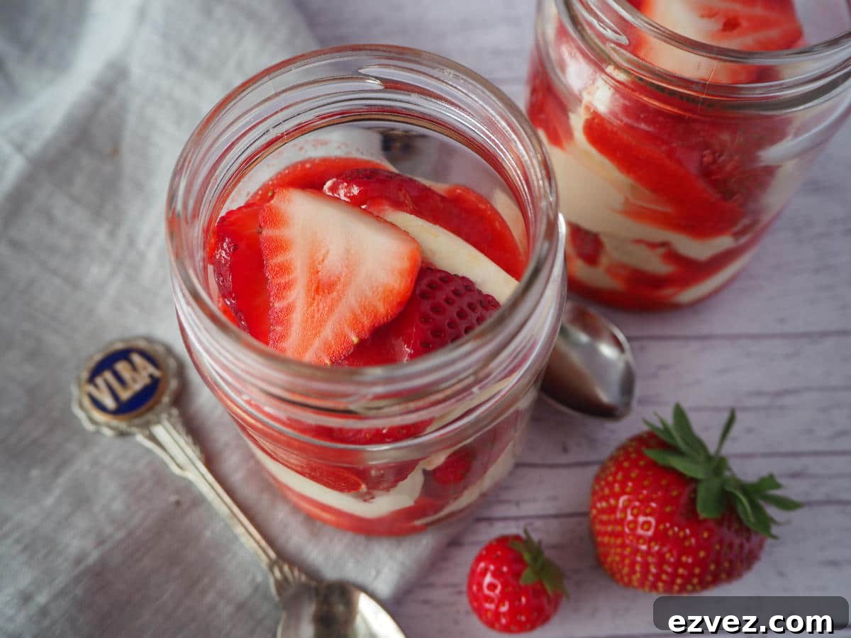 Two jars of Eton mess with fresh strawberries on the side, spoons and a linen cloth.