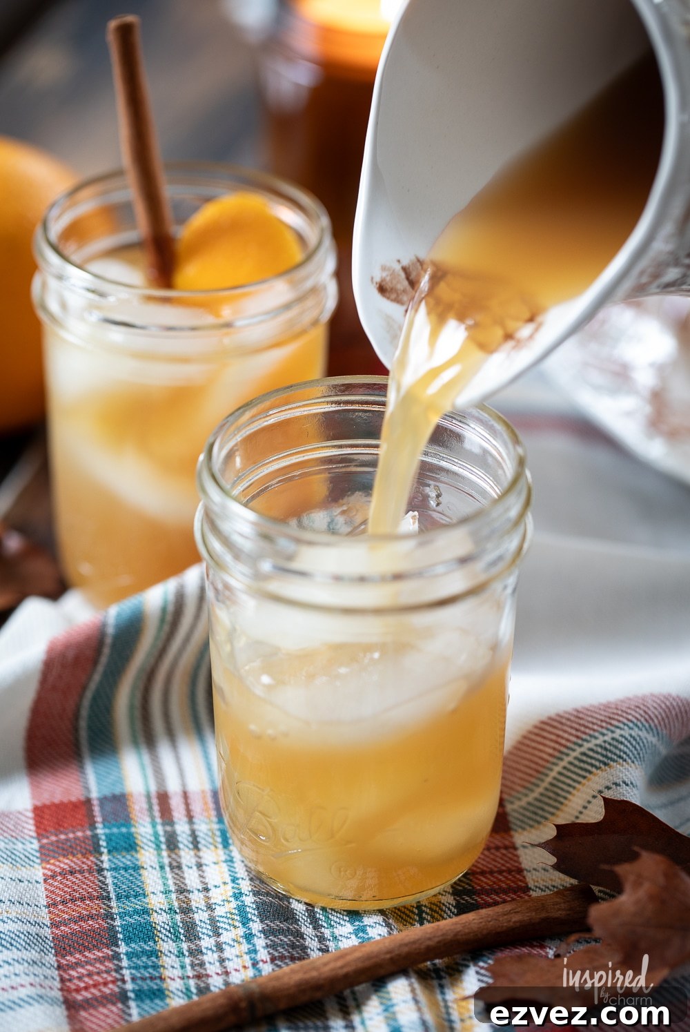 white pitcher pouring apple cider mixture into jar with ice.