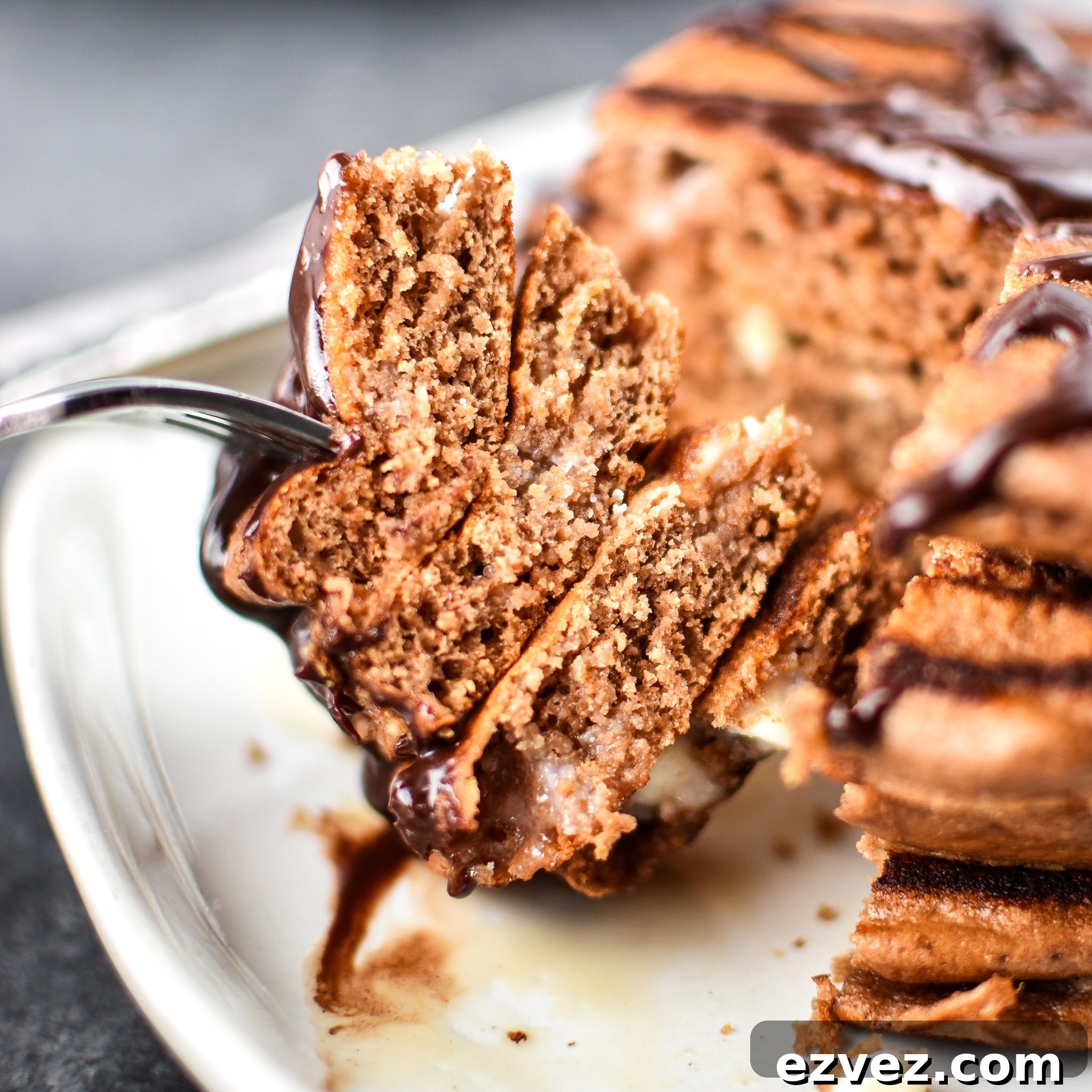 A fork piercing a big stack of Double Chocolate Peppermint Protein Pancakes drizzled with chocolate syrup.