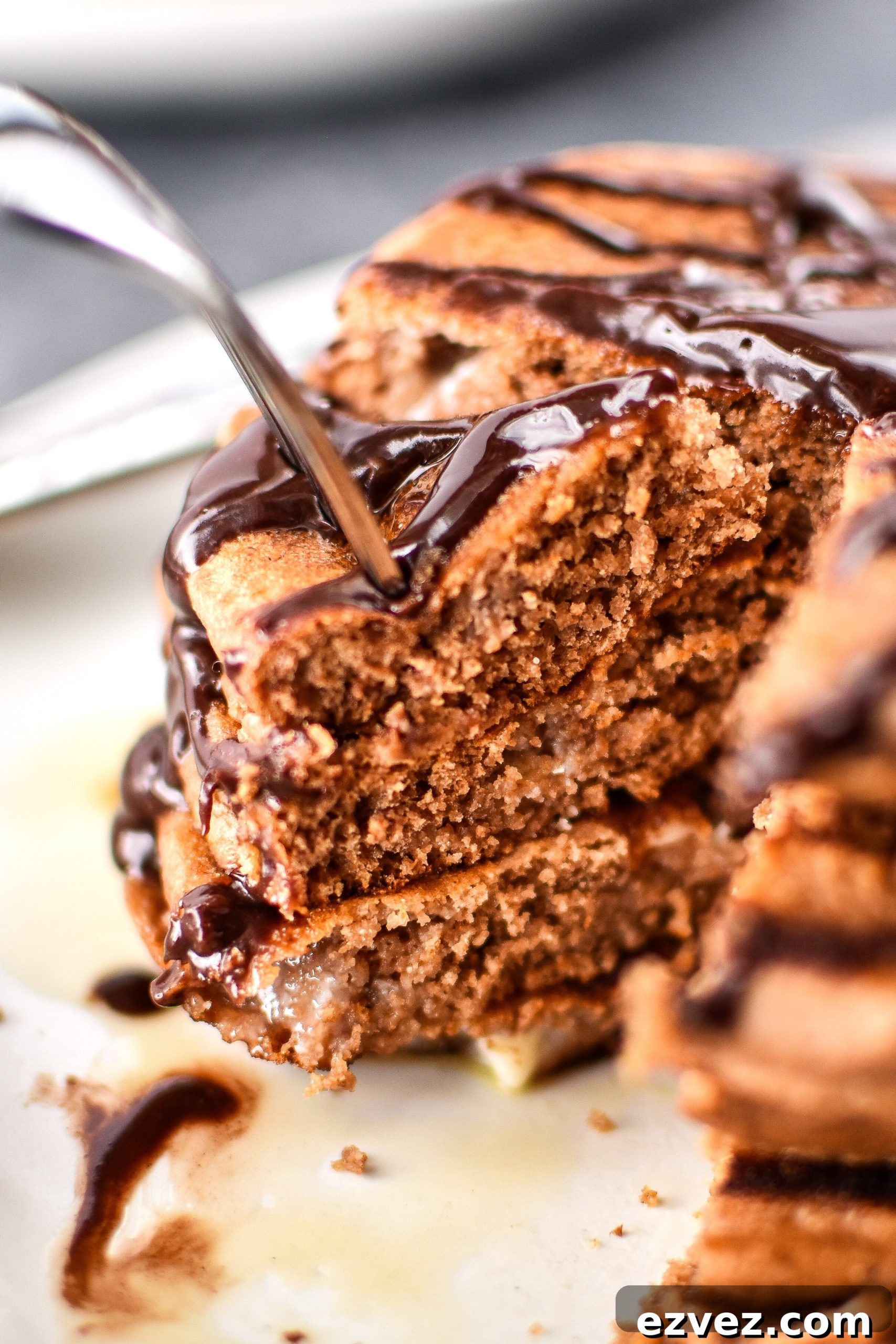 A fork piercing a big stack of Double Chocolate Peppermint Protein Pancakes drizzled with chocolate syrup.