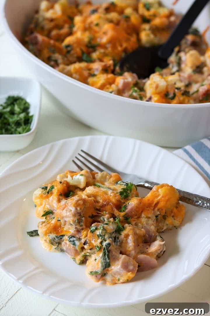 Creamy Ham and Rice Casserole Made with Leftover Ham 2 Portrait image of leftover ham casserole served on a white plate and the casserole dish in the background. Casserole is right out of the oven with melted cheese, bits of ham and vegetables, and it's garnished with fresh parsley.