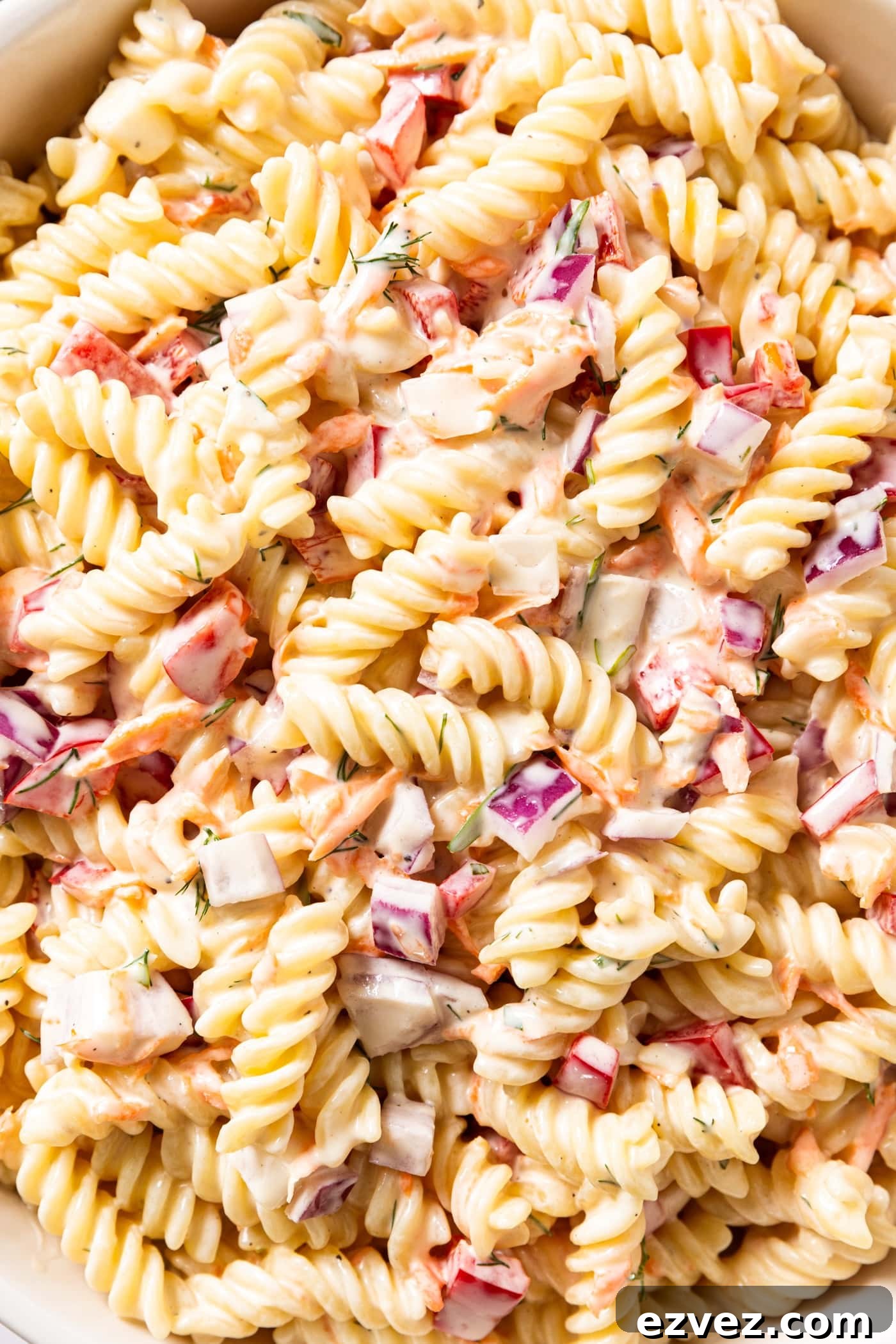 Cooked pieces of pasta covered in creamy dressing tossed with pieces of red pepper, red bell pepper, and grated carrot.