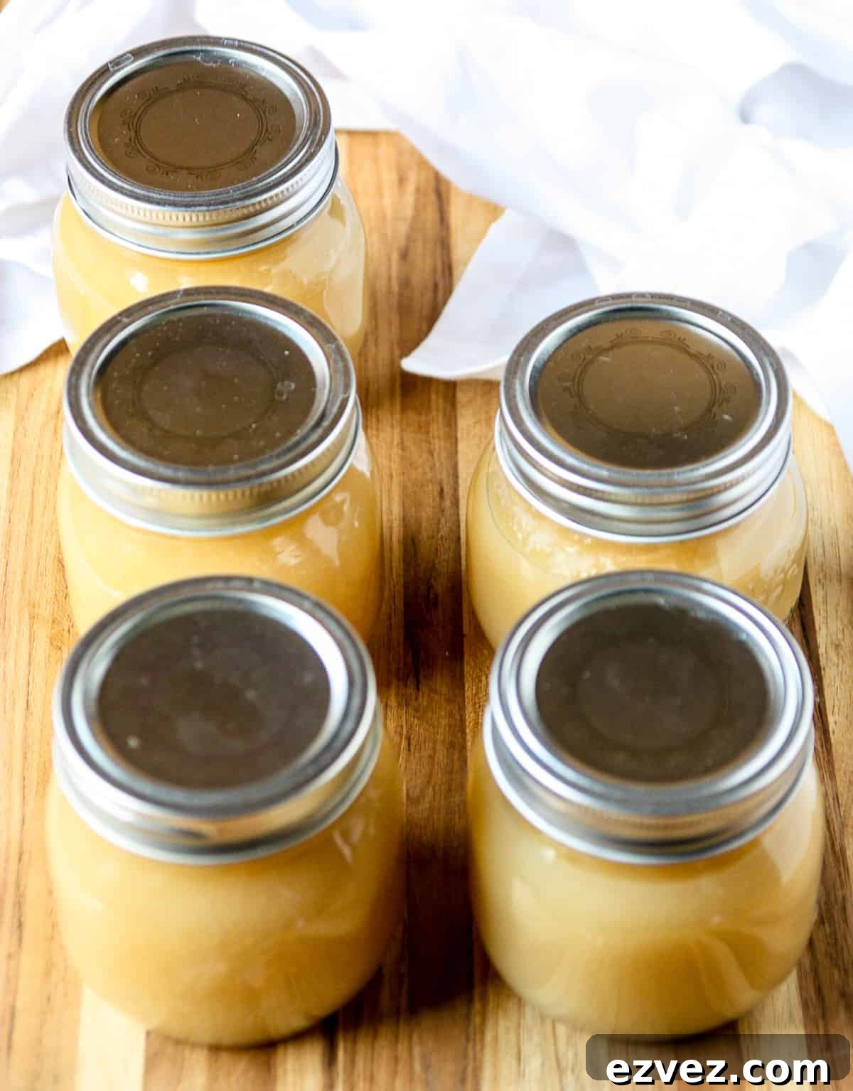 Five processed jars of applesauce on a wooden board.