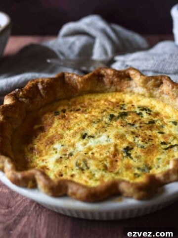 Angled view of tomato, leek and feta quiche on a brown surface with tomatoes and a linen in the background