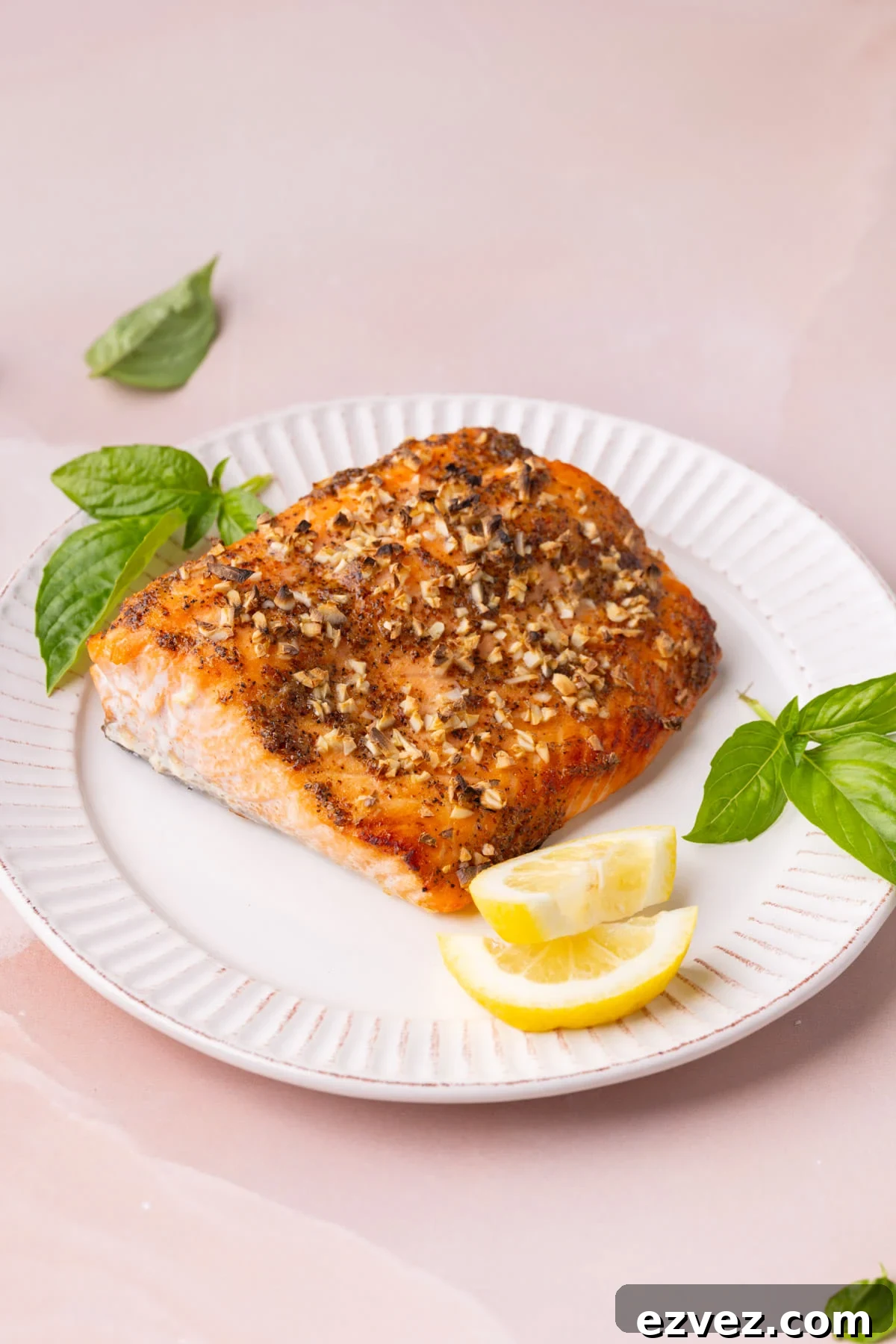 Roasted salmon with honey and mustard topped with garlic and plated with fresh basil and lemon wedges. 