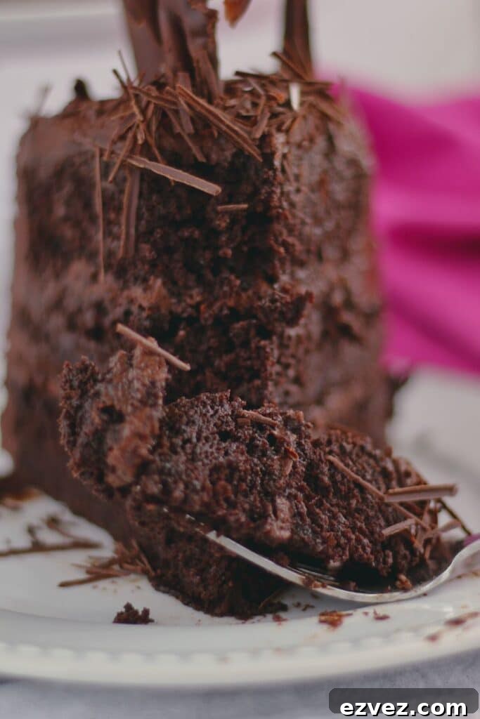Decadent Gluten-Free Chocolate Cake Recipe for Perfect Texture 19 fork full of chocolate cake in front of slice on white plate with hot pink cloth napkin in the background.