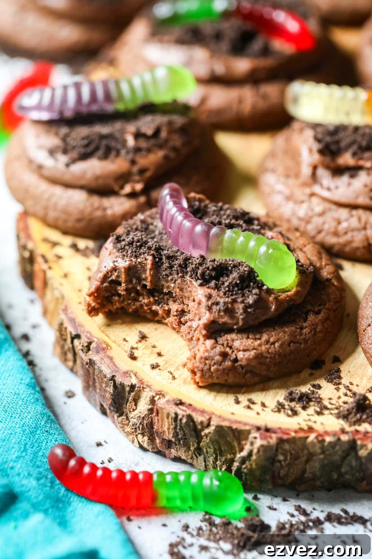 Bite missing from a chocolate cookie topped with Oreo crumbs and gummy worms.
