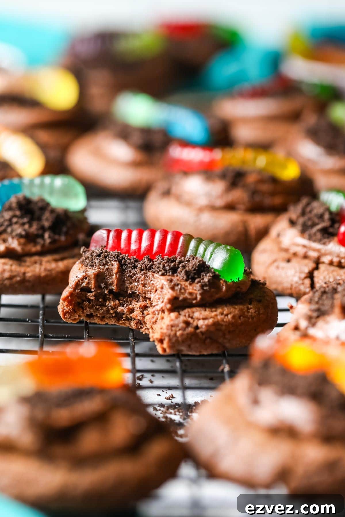 Bite missing from a chocolate cookie topped with Oreo crumbs and gummy worms.