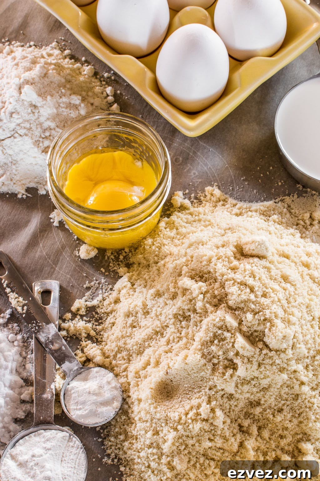 A table of baking ingredients with flours, eggs, and measuring spoons.