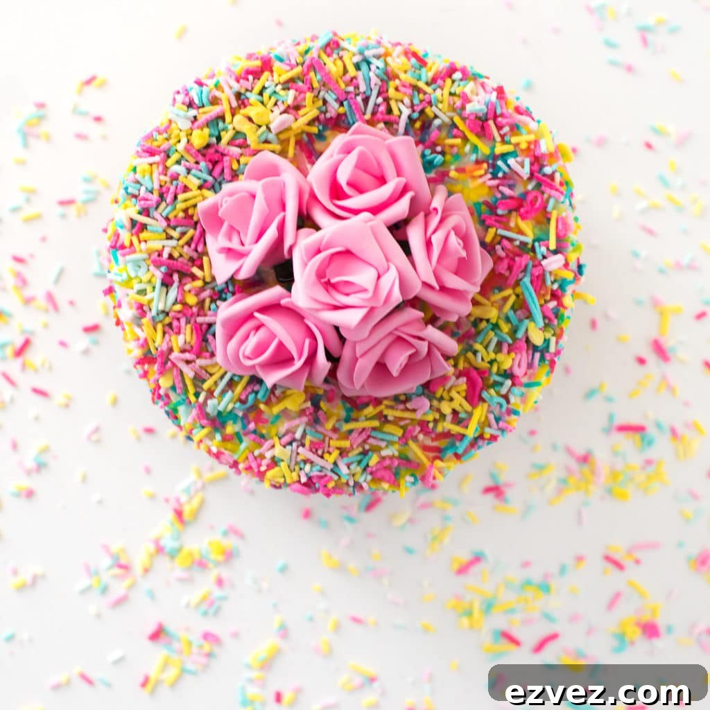 Overhead photo of a cake coated in sprinkles with pink flowers on top. 