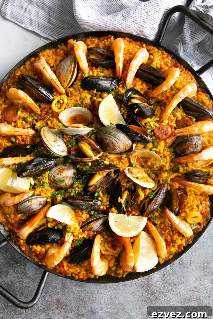 Overhead of seafood paella in large, handled serving bowl on gray background.