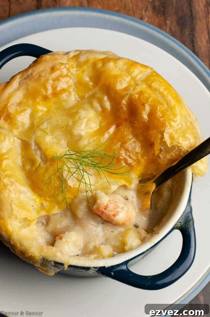 Overhead of individual Thanksgiving pot pie in enameled blue croock with part of the top crust gone and a spoon dipping into filling.