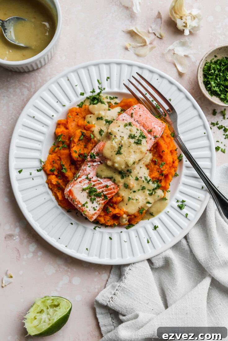 Overhead of the salmon presented on mashed sweet potatoes with gravy drizzled atop on a white rimmed late with fork, and extra ingredients at edges of photo.