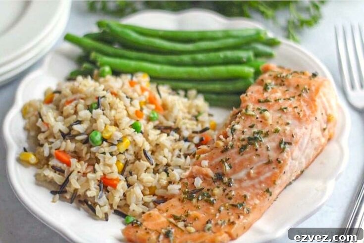 one slice of salmon on decorative white plate with a portion of rice pilaf and green beans.