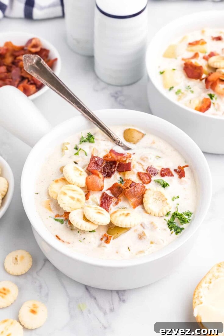 Spoon dipped into single serving of chowder in white bowl with second bowl and various garnishes nearby.
