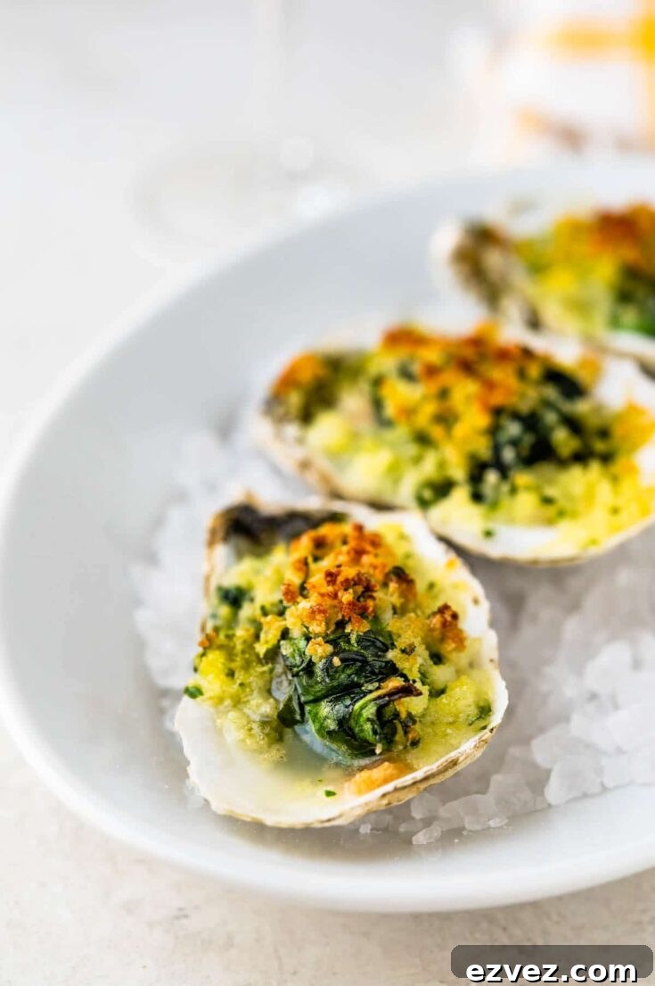 Closeup of one oyster with others behind, presented on ice chips in oval white bowl.